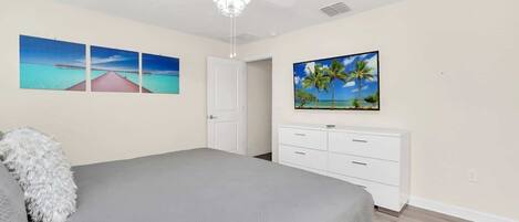 A bedroom with a bed, a ceiling fan, a white dresser, and two wall-mounted paintings.