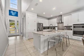 A modern kitchen with white cabinetry, stainless steel appliances, and a central island with bar stools. - The Gathering Spot - Six Bedroom House, Sleeps 14 (Lake Buena Vista)