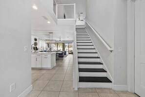 A modern interior with a staircase leading to an upper level, a kitchen area with white cabinetry, and a dining space with a table and chairs. - Outdoor Kitchen - Pool and Hot Tub - Imaginative Themed Bedrooms -Arcade Machine (Lake Buena Vista)
