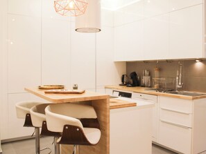 Una cocina moderna con armarios blancos, una isla de madera, taburetes de bar y una lámpara colgante.