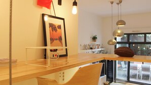 Ein modernes Wohnzimmer mit einem Holztisch, einem gerahmten Bild an der Wand und Blick ins Freie durch große Fenster.