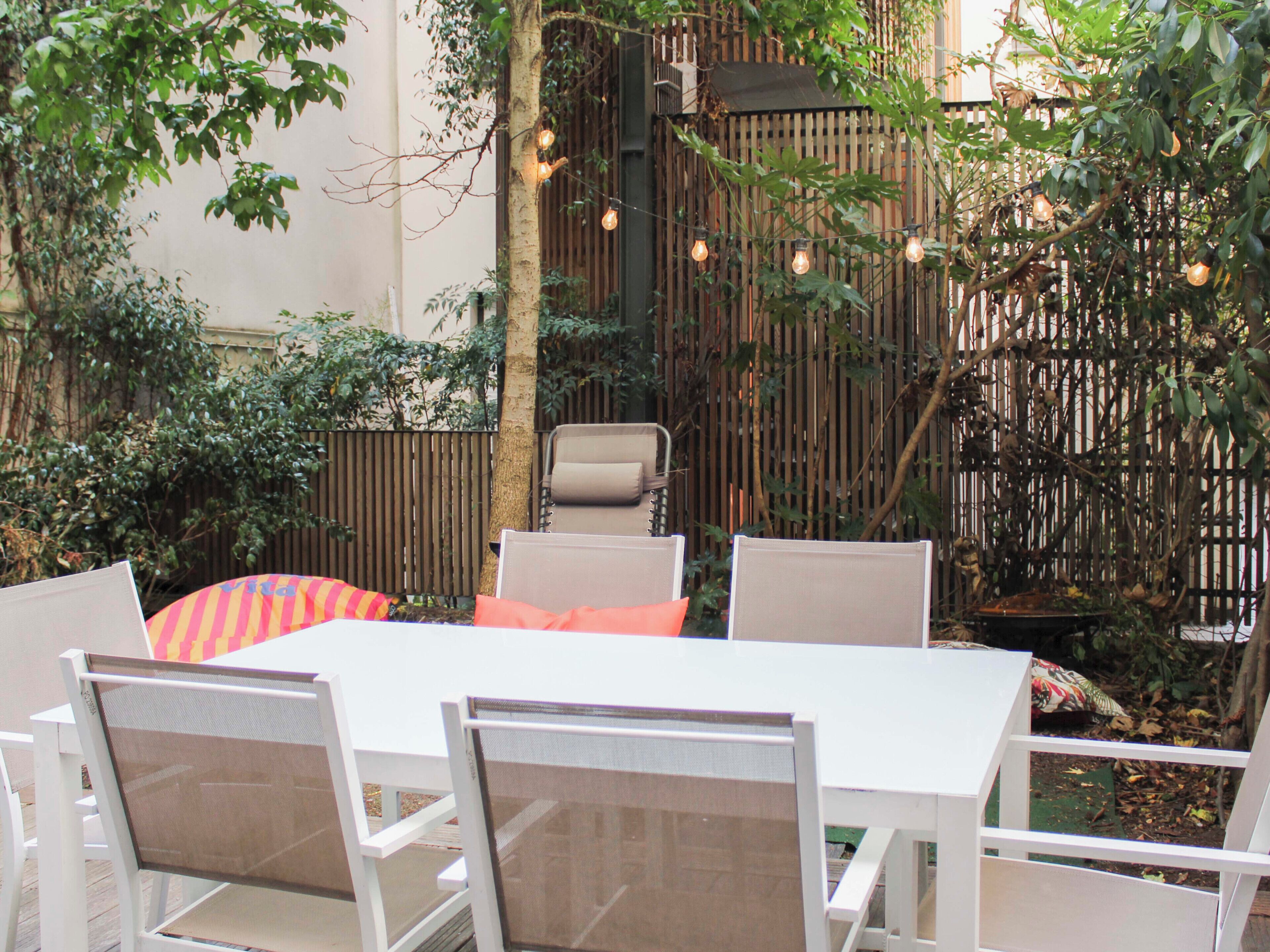 Eine Terrasse im Freien mit einem weißen Tisch und Stühlen, umgeben von Pflanzen und einem Bambuszaun.