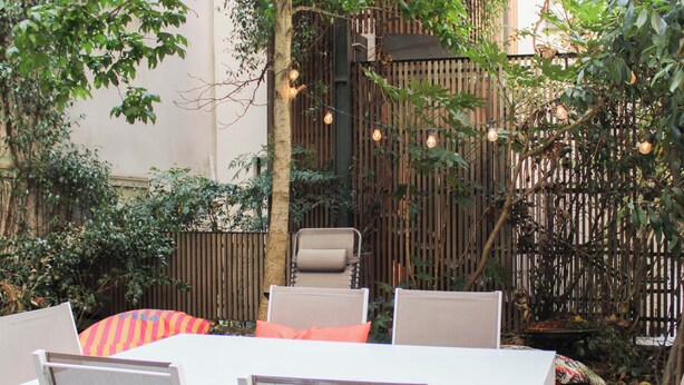 Eine Terrasse im Freien mit einem weißen Tisch und Stühlen, umgeben von Pflanzen und einem Bambuszaun.