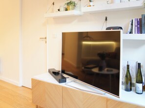 A flat-screen TV mounted on a white wall, with a wooden cabinet below and a shelf above holding books and decorative items. - Apartment with terrace and garden – sleeps 4 (Paris)