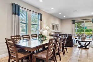 A dining area with a glass table and wooden chairs, a sofa, and a small round table with a lamp. - Private Pool and Jetted Tub/Private Cinema/Close to Disney/Spacious pool deck (Kissimmee)