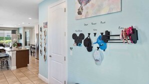 A hallway with a light blue wall, a door, and a wall-mounted display of various hats and bags. - The Memory Box - Eight Bedroom House, Sleeps 20 (Kissimmee)