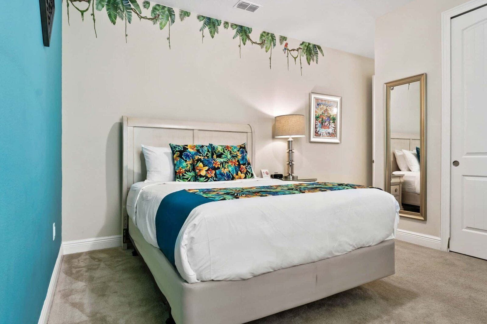 A bedroom with a bed, a nightstand, a lamp, a framed picture, and a door.