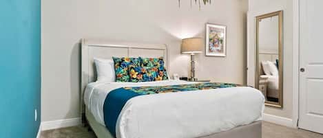 Un dormitorio con cama, mesita de noche, lámpara, cuadro enmarco y puerta.