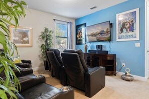 A living room with a large flat-screen TV, reclining chairs, a small table, and a decorative item on the floor. - Private Pool and Jetted Tub/Private Cinema/Close to Disney/Spacious pool deck (Kissimmee)