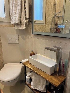 A bathroom with a white toilet, a wooden vanity with a white sink, and a mirror above the sink. - Charming T2 Batignolles with private courtyard (Paris)