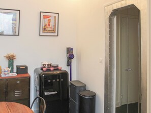 A room with a wooden table, a water dispenser, a trash bin, a framed picture, and a door. - Charming T2 Batignolles with private courtyard (Paris)