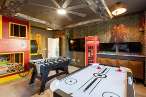 Una stanza con un tavolo da calcio, una cabina telefonica rossa e un muro con un grande schermo televisivo.
