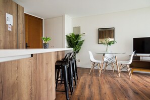 Una cocina moderna con armarios de madera, una encimera blanca y un comedor con mesa y sillas de vidrio.
