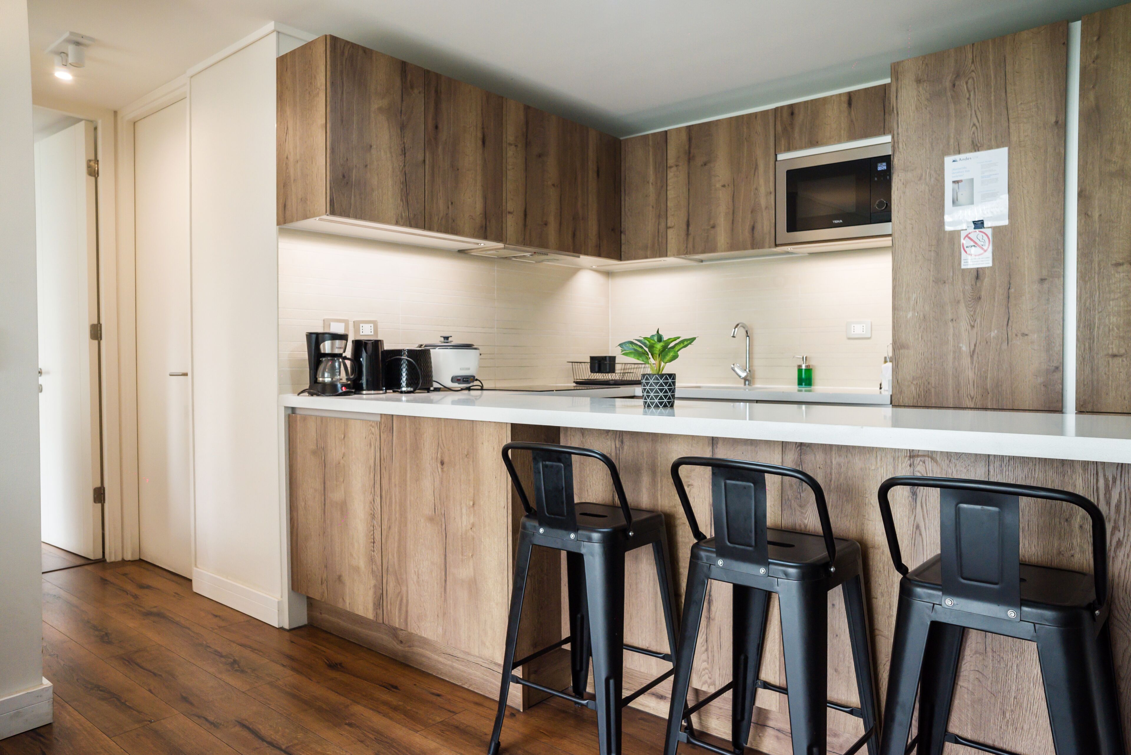 A modern kitchen with wooden cabinetry, a white countertop, and two black bar stools.