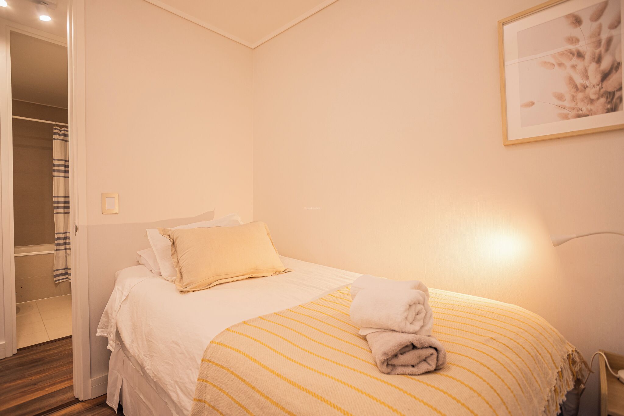 A hotel room with a bed, a bedside lamp, a towel, and a framed picture on the wall.