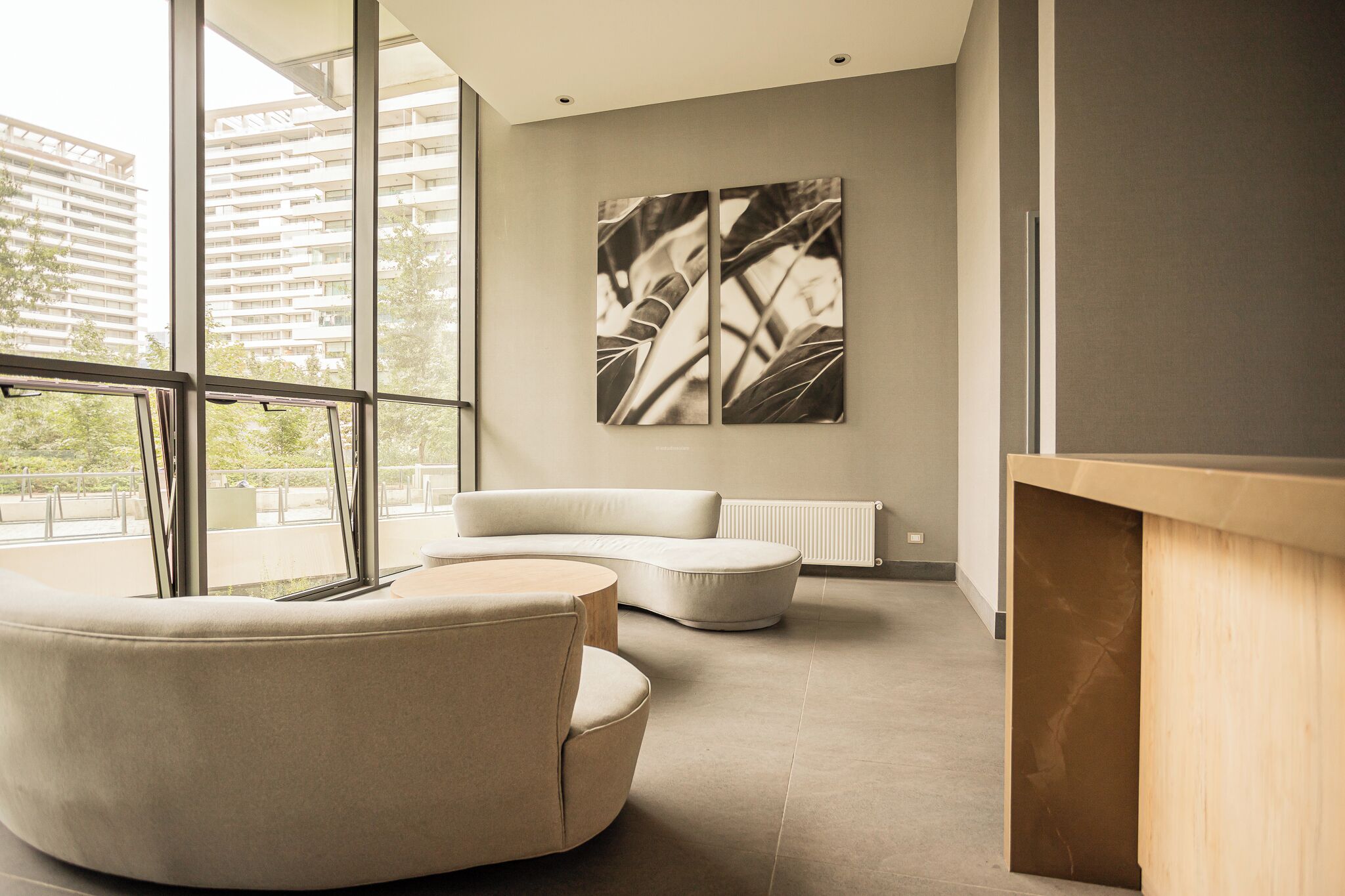 A modern interior with a curved sofa, a wooden desk, and large windows offering a view of buildings.