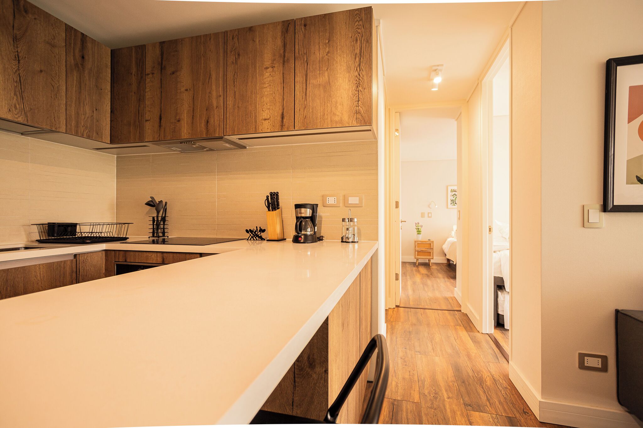 A modern kitchen with wooden cabinets, a white countertop, and a coffee maker.