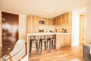 A modern kitchen with wooden cabinets, a built-in microwave, and a bar area with stools. - Manquehue Norte Apartments by Andes STR (Las Condes)