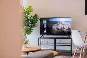 Ein Fernseher auf einem Schrank mit Netflix-Anzeige, eine Zimmerpflanze und ein weißer Stuhl.