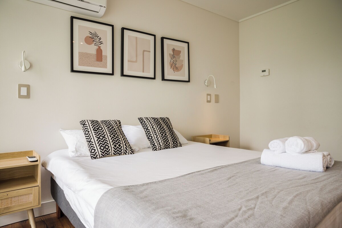 Ein Hotelzimmer mit Bett, Nachttischen, einer Wand-Klimaanlage und gerahmten Kunstwerken.