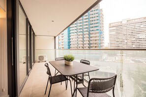 Ein Balkon mit Tisch und Stühlen, einer Kübelpflanze und Blick auf hohe Gebäude.