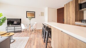 Eine moderne Küche mit Holzschränken, einer weißen Arbeitsplatte und einem Essbereich mit einem Glastisch und Stühlen.