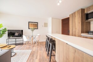 Eine moderne Küche mit Holzschränken, einer weißen Arbeitsplatte und einem Essbereich mit einem Glastisch und Stühlen.