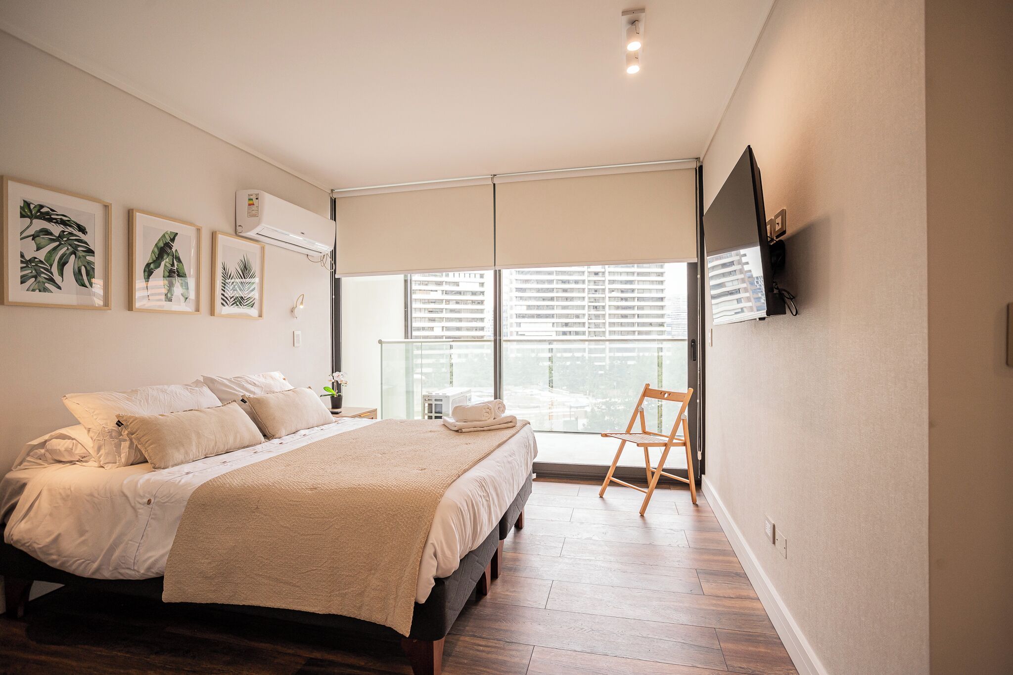 Un dormitorio con cama, una silla, un ventanal y obras de arte en la pared.