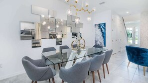 A modern dining area with a glass table, grey upholstered chairs, and a blue velvet chair. - Cool Breeze - Four Bedroom House, Sleeps 9 (Kissimmee)