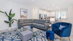 A modern living room with a grey sectional sofa, a blue armchair, a glass coffee table, and a patterned rug. - Private Pool/Clubhouse/Restaurant & Bar/7 miles Disney/Splash Park/Free Wifi (Kissimmee)