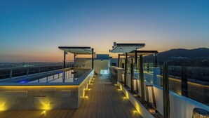 Eine Dachterrasse mit Pool, Sitzgelegenheiten und Blick auf die Abendstadt.