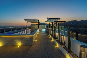 A rooftop terrace with a pool, seating areas, and a view of the cityscape at dusk. - Villa Soho, your own boutique hotel in Cabo (Cabo San Lucas)