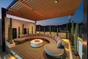 A modern outdoor seating area with a curved sofa and a central fire feature, surrounded by cacti. - Villa Soho, your own boutique hotel in Cabo (Cabo San Lucas)