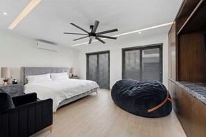 A modern bedroom with a bed, a ceiling fan, a bean bag, and large windows with blinds. - Villa Soho, your own boutique hotel in Cabo (Cabo San Lucas)