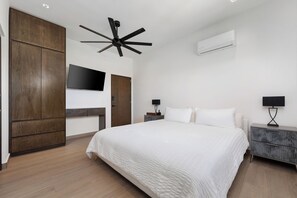 A modern bedroom with a large bed, a ceiling fan, a flat-screen TV, and a built-in air conditioning unit. - Villa Soho, your own boutique hotel in Cabo (Cabo San Lucas)