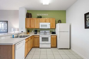 A compact kitchen with wooden cabinets, a microwave, a stove, and a refrigerator. - Firefly Cottage - Four Bedroom Apartment, Sleeps 8 (Kissimmee)