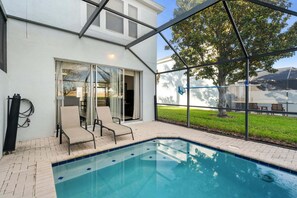 A swimming pool with a glass enclosure, two lounge chairs, and a hose reel. - Firefly Cottage - Four Bedroom Apartment, Sleeps 8 (Kissimmee)