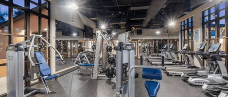 A gym with various exercise equipment, large windows, and a high ceiling.