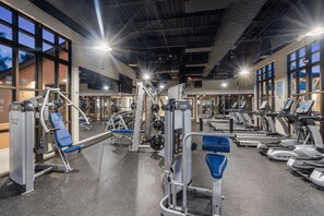 Ein Fitnessstudio mit verschiedenen Trainingsgeräten, großen Fenstern und hoher Decke.