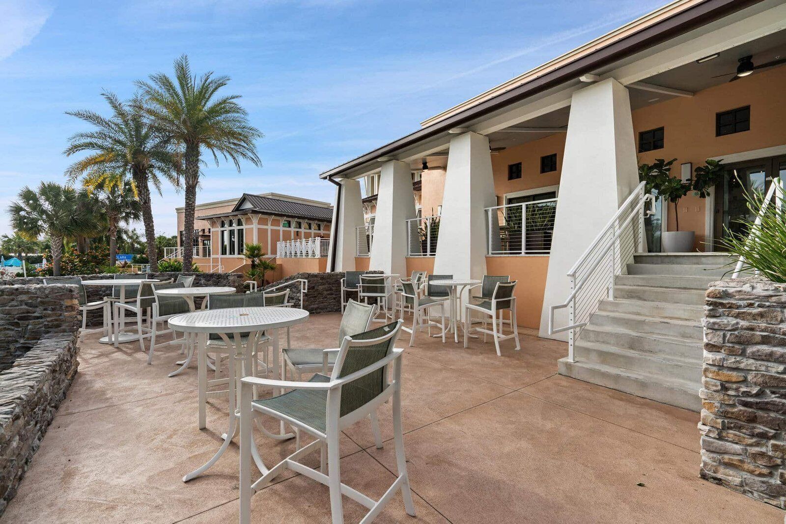 Un espace extérieur aménagé en terrasse, avec des tables et des chaises, un mur en pierre et un bâtiment doté d’un escalier.