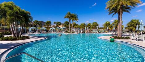 A large outdoor swimming pool with clear blue water, surrounded by palm trees and lounge chairs.