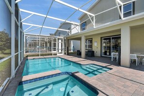 Una piscina con un porche cubierto, mobiliario exterior y vistas de los edificios circundantes.