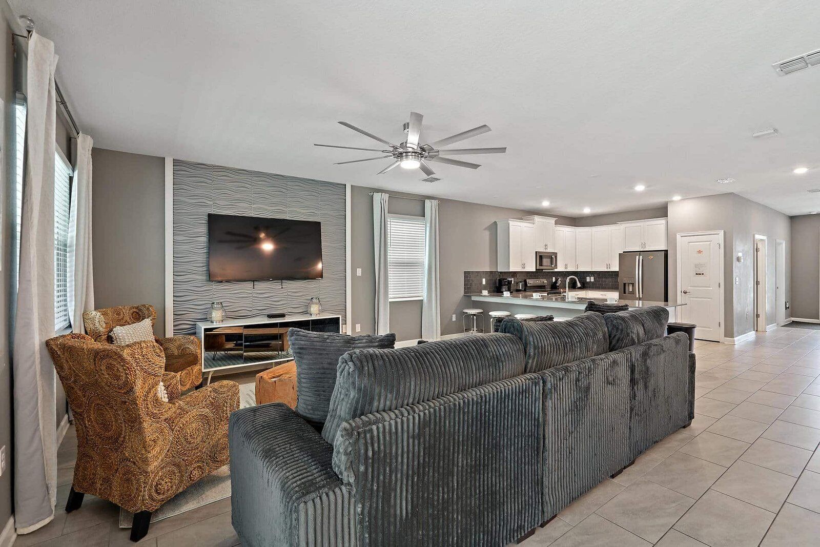 A modern living room with a large sectional sofa, a television, and a ceiling fan.