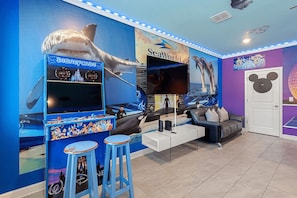 Habitación con un gran mural en la pared, un letrero de SeaWorld, un televisor, un sofá y una puerta con motivos de Mickey Mouse.