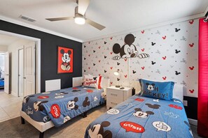 Ein Zimmer mit zwei Betten, einem Deckenventilator, einer Mickey Mouse Wandsticker und einem Mickey Mouse Kopfkissen.