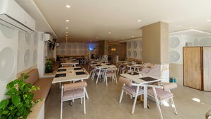 Ein geräumiges Restaurant mit mehreren Tischen und Stühlen, abgehängten Deckenleuchten und einem modernen Innenraum.