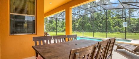 Alpendre coberto com mesa de bilhar, cadeiras e vista para uma piscina e vegetação.