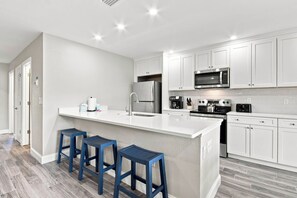 Una cocina moderna con armarios blancos, electrodomésticos de acero inoxidable y una isla central con taburetes de bar.