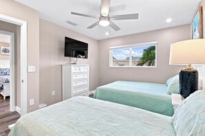 A hotel room with two beds, a ceiling fan, a TV mounted above a dresser, and a window with a view. - Relaxing Unit K2 · Sanibel Arms West | Easy 2 Minute Walk to the Beach (Sanibel)