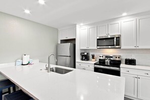 A modern kitchen with white cabinetry, stainless steel appliances, and a central island with a sink. - Relaxing Unit K2 · Sanibel Arms West | Easy 2 Minute Walk to the Beach (Sanibel)